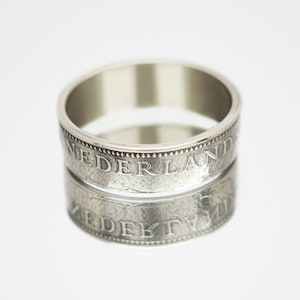 May include: A silver ring made from two stacked Dutch coins. The coins feature the inscription "NEDERLAND" around the edge.