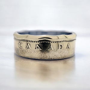 May include: A gold-toned ring made from a Canadian coin. The ring features the word "CANADA" embossed on the band.