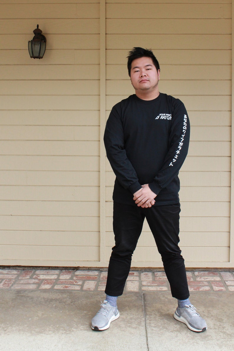 May include: A person wearing a black long-sleeved shirt with white text that reads "YOUR VIBE ATTRACTS YOUR TRIBE" on the right sleeve and black pants. The person is wearing gray sneakers.