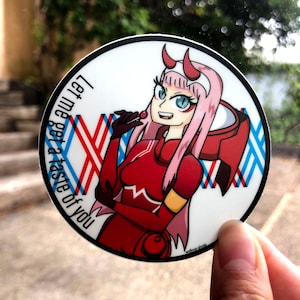May include: A round sticker featuring an anime character with pink hair and a red and white suit. The character is holding a lollipop and has a mischievous expression. The sticker has the text "Let me get a taste of you" written around the edge.