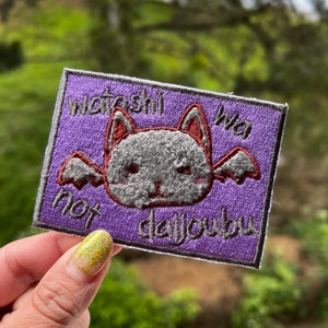 May include: Purple embroidered patch with a gray bat with red ears and wings. The text on the patch reads "watashi wa not daijoubu".