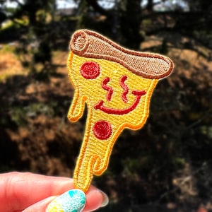 May include: A yellow and red embroidered iron-on patch of a slice of pizza with a smiling face and dripping cheese.