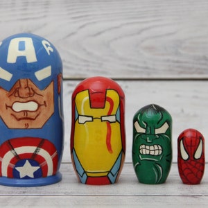 Puede incluir: Conjunto de cinco muñecas rusas, cada una pintada con un personaje de superhéroe diferente: Capitán América, Iron Man, Hulk, Spiderman y una muñeca más pequeña con la letra 'A'.