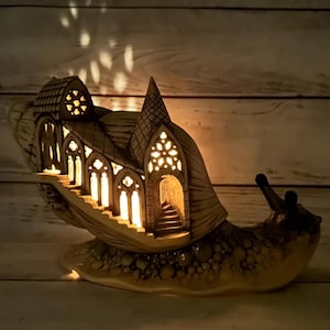 Könnte beinhalten: Eine Holzskulptur einer Schnecke mit einer detaillierten, beleuchteten gotischen Kathedrale auf ihrem Rücken. Die Schnecke ruht auf einer Holzoberfläche.