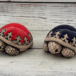 Könnte beinhalten: Zwei Keramik-Schildkröten-Figuren, eine rote und eine blaue, mit aufwendigen Designs auf ihren Schalen.