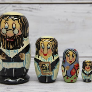 Pode incluir: Conjunto de cinco bonecas russas tradicionais, ou bonecas matrioska, pintadas com desenhos coloridos. A boneca maior representa um homem com barba e óculos, enquanto as bonecas menores representam mulheres com diferentes expressões faciais e roupas.
