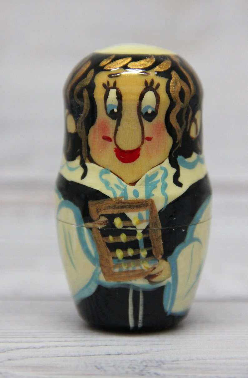 May include: A hand-painted wooden nesting doll, or matryoshka, depicting a woman with brown hair and a blue and white dress holding an abacus. The doll is painted in a whimsical style with a bright yellow background.