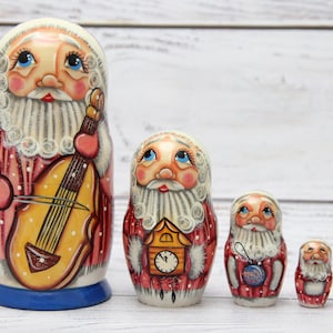 May include: Set of five traditional Russian nesting dolls, or matryoshka dolls, featuring Father Christmas in various poses. The largest doll is holding a violin, the second largest has a cuckoo clock, the third has a Christmas ornament, the fourth has a bell, and the smallest is a green Christmas tree.