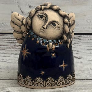 May include: A ceramic angel figurine with a blue and gold starry design. The angel has a white face with painted features and a blue and gold crown.