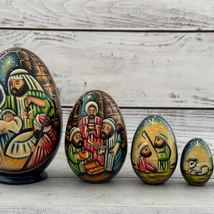 Peut inclure: Ensemble de cinq œufs russes en bois peints à la main, représentant des scènes de la Nativité. Le plus grand œuf montre Marie, Joseph et l'enfant Jésus. Les œufs sont de tailles variées, avec des œuvres d'art détaillées et une finition brillante.