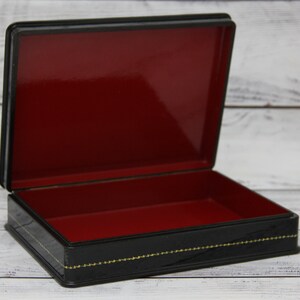 May include: Black lacquered wooden box with a red velvet interior. The box has a gold trim and a decorative design.