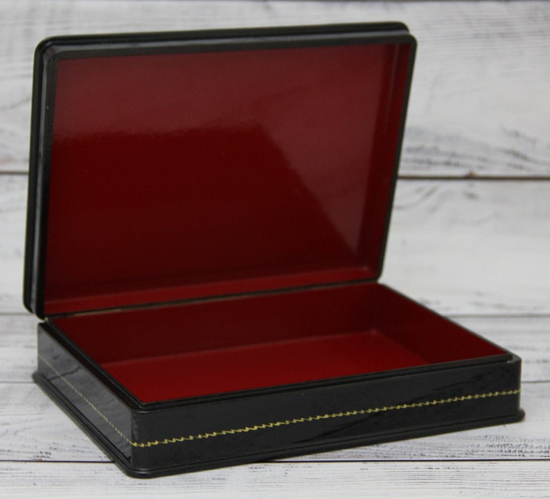 May include: Black lacquered wooden box with a red velvet interior. The box has a gold trim and a decorative design.