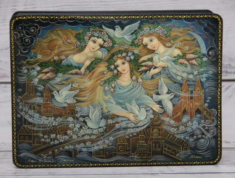 May include: A hand-painted wooden box with a scene of three women with long flowing hair and white doves flying around them. The women are wearing floral crowns and flowing white dresses. The background is a dark blue sky with clouds and a city skyline.