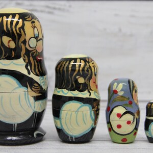 May include: Set of five traditional Russian nesting dolls, or matryoshka dolls. The largest doll is painted with a man wearing a black coat and white shirt. The other dolls are painted with women wearing colorful dresses.
