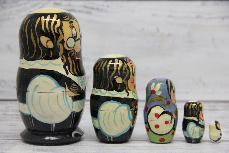 May include: Set of five traditional Russian nesting dolls, or matryoshka dolls. The largest doll is painted with a man wearing a black coat and white shirt. The other dolls are painted with women wearing colorful dresses.