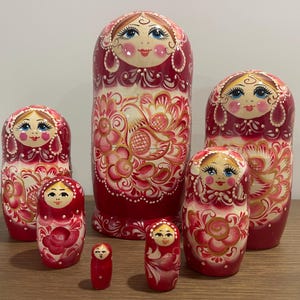 May include: A set of traditional Russian nesting dolls, also known as matryoshka dolls. The dolls are painted in a red, white, and gold color scheme with floral designs. The largest doll is the tallest and the smallest doll is the shortest.