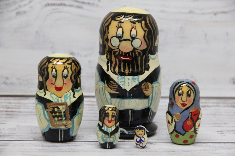 May include: Set of five traditional Russian nesting dolls, or matryoshka dolls. The largest doll is a man with a beard and glasses, wearing a black and white outfit. The other dolls are a woman with a calculator, a woman with a blue dress, a woman with a black dress, and a small woman with a blue dress.