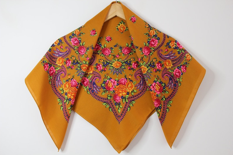 May include: A mustard yellow square scarf with a floral pattern in shades of pink, orange, purple, and green.
