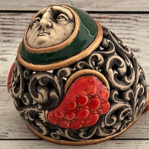May include: A ceramic figurine with a detailed face and intricate floral designs. The figurine is painted in shades of green, red, and gold.