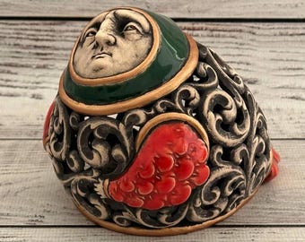May include: A ceramic figurine with a detailed face and intricate floral designs. The figurine is painted in shades of green, red, and gold.