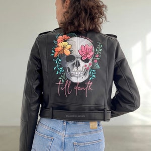 Puede incluir: Chaqueta de cuero negra con un diseño de calavera y flores en la espalda. La calavera está rodeada de flores en tonos rosa, naranja y amarillo. El texto "till death" está escrito en rosa debajo de la calavera. La chaqueta tiene una cremallera y un cinturón en la cintura.