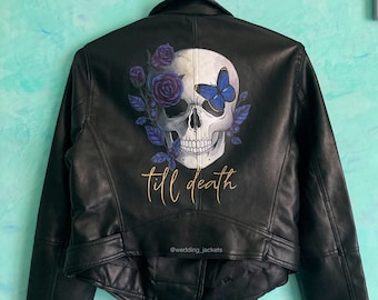 May include: Black leather jacket with a painted skull design on the back. The skull has one eye replaced with a blue butterfly and is surrounded by purple flowers. The text "till death" is written in gold below the skull.