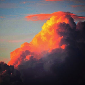 May include: A dramatic sunset sky with dark clouds illuminated by a bright orange glow. The clouds are layered and textured, creating a sense of depth and movement.