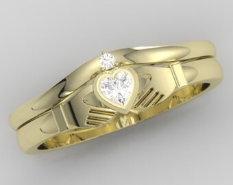 May include: A gold-colored Claddagh ring set. The engagement ring features a heart-shaped diamond held by hands, with a small diamond above. The wedding band is a simple gold band. The rings are displayed on a light gray background.
