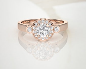 May include: A rose gold engagement ring with a round center stone surrounded by smaller diamonds. The ring has two smaller diamonds on the band.