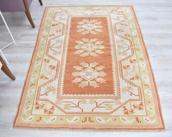 May include: A traditional Turkish rug with a geometric pattern in shades of orange, beige, and green. The rug has a central medallion and a border with floral motifs.