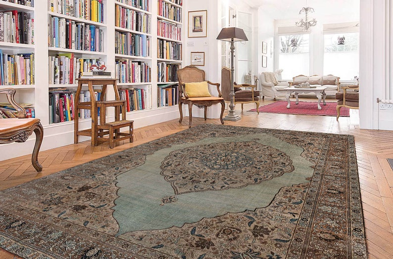 Pu&ograve; includere: Un tappeto a motivi blu chiaro e marrone con un grande e intricato disegno floreale al centro. Il tappeto &egrave; steso su un pavimento in legno in una stanza con pareti bianche e librerie.