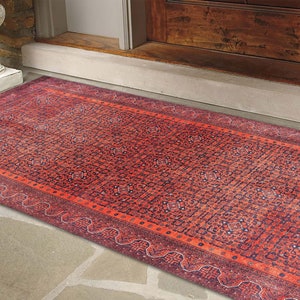 May include: A red and blue patterned rug with a geometric design. The rug is placed on a stone floor in front of a wooden door.