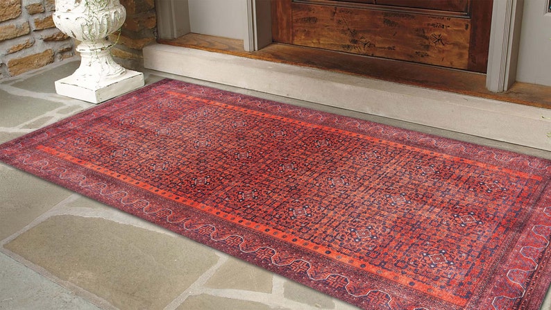May include: A red and blue patterned rug with a geometric design. The rug is placed on a stone floor in front of a wooden door.