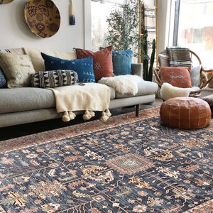 K&ouml;nnte beinhalten: Ein Wohnzimmer mit einem grauen Sofa, einem gemusterten Teppich und einer Auswahl an Kissen. Der Teppich hat einen dunkelblauen Hintergrund mit komplizierten Mustern in Orange-, Rot- und Gr&uuml;nt&ouml;nen.
