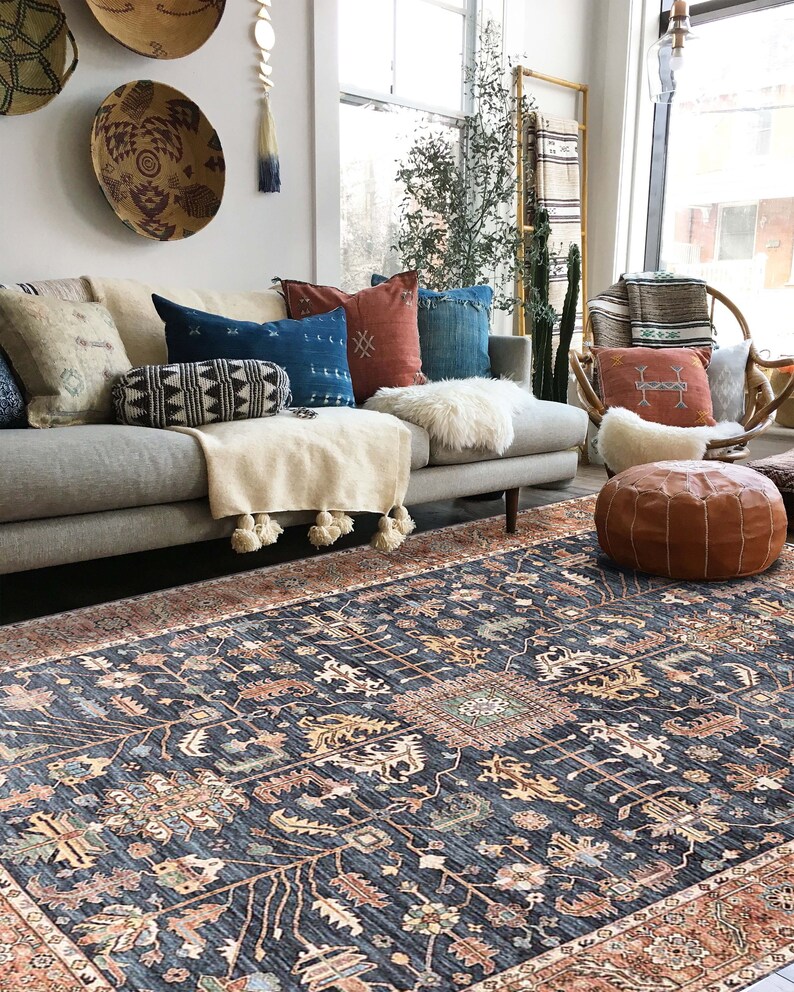 K&ouml;nnte beinhalten: Ein Wohnzimmer mit einem grauen Sofa, einem gemusterten Teppich und einer Auswahl an Kissen. Der Teppich hat einen dunkelblauen Hintergrund mit komplizierten Mustern in Orange-, Rot- und Gr&uuml;nt&ouml;nen.