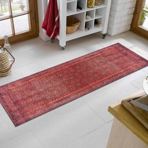 May include: A red and orange patterned runner rug with a dark blue border. The rug is laid out on a white tiled floor.