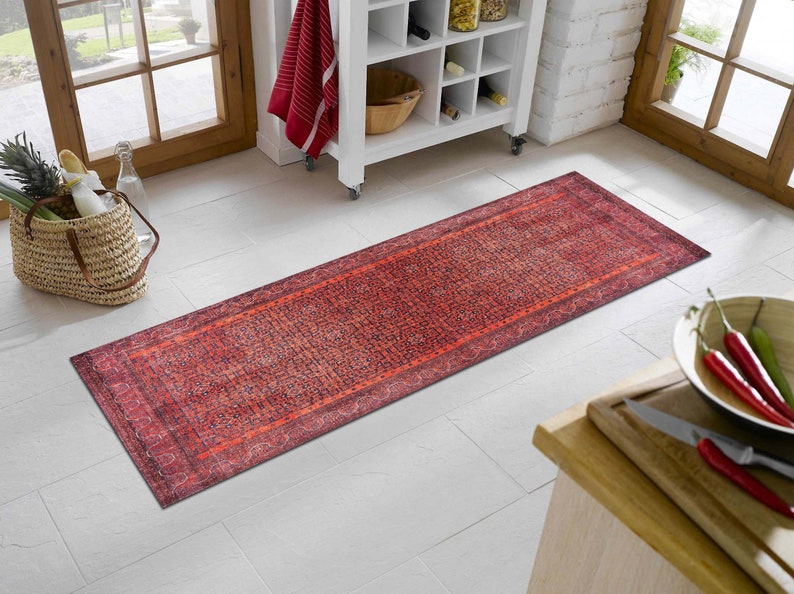May include: A red and orange patterned runner rug with a dark blue border. The rug is laid out on a white tiled floor.