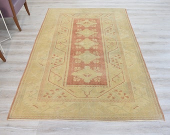May include: A vintage rug with a beige background and a central rectangular panel in a muted orange color. The rug features a repeating floral pattern throughout.