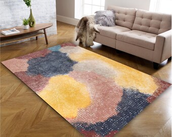 May include: A rectangular area rug featuring an abstract pattern of large, overlapping organic shapes in shades of navy blue, mustard yellow, dusty rose, and cream. The surface has a subtle, fine-textured grid overlay across the entire design.