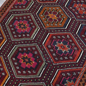 Pu&ograve; includere: Un tappeto rosso, arancione e blu con un motivo geometrico. Il tappeto ha un bordo a frange.