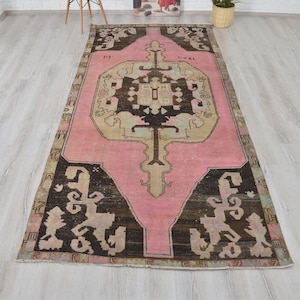 May include: A vintage rug in pink and brown with a geometric pattern. The rug features a central medallion with a floral design and a border with a repeating pattern.
