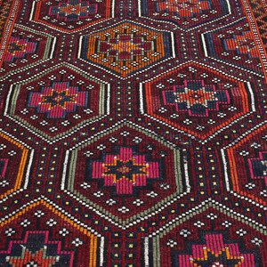 Pu&ograve; includere: Un tappeto turco tradizionale con un motivo geometrico in tonalit&agrave; di rosso, arancione, verde e nero. Il tappeto ha un design dettagliato con dettagli intricati e una trama tessuta.