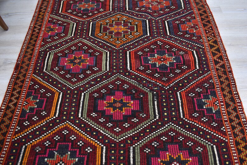 Pu&ograve; includere: Un tappeto turco tradizionale con un motivo geometrico in tonalit&agrave; di rosso, arancione, verde e nero. Il tappeto ha un design dettagliato con dettagli intricati e una trama tessuta.
