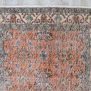 May include: A rectangular area rug featuring a central field of burnt orange with intricate floral and geometric patterns in shades of blue, green, and cream. The rug is framed by a wide decorative border and finished with a short white fringe.