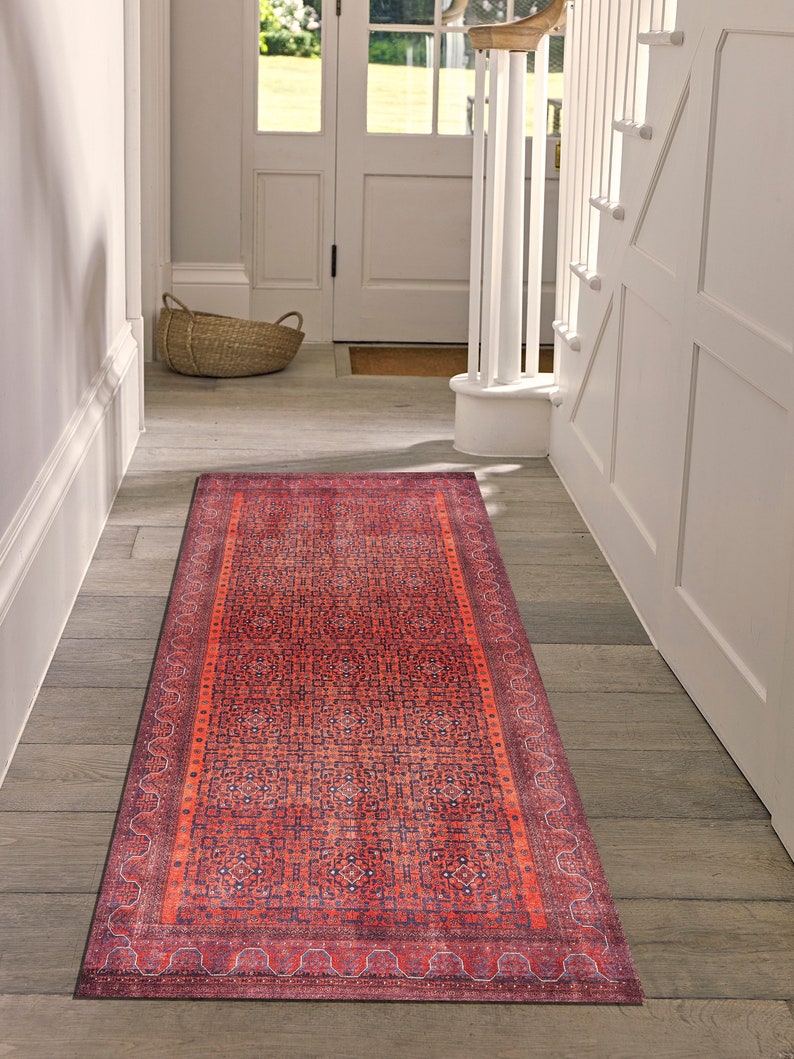 May include: A red and blue patterned runner rug with a geometric design. The rug is placed in a hallway with white walls and wooden floors.