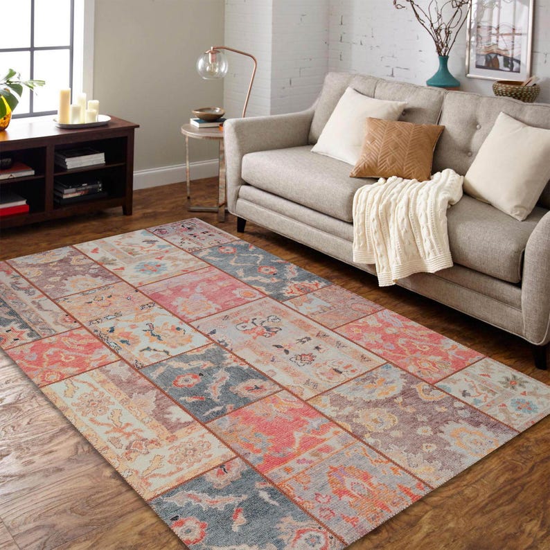 May include: A rectangular area rug with a patchwork design. The rug features a variety of floral and geometric patterns in shades of pink, blue, and beige. The rug is placed on a hardwood floor in a living room setting.