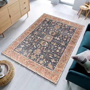K&ouml;nnte beinhalten: Ein dunkelblauer Teppich mit traditionellem persischem Design. Der Teppich hat einen cremefarbenen und rostbraunen Rand mit komplizierten Blumenmustern. Der Teppich liegt auf einem hellen Holzboden.