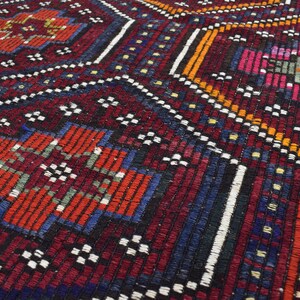 Pu&ograve; includere: Primo piano di un tappeto tessuto colorato con intricati motivi geometrici in tonalit&agrave; di rosso, blu, arancione e bianco.