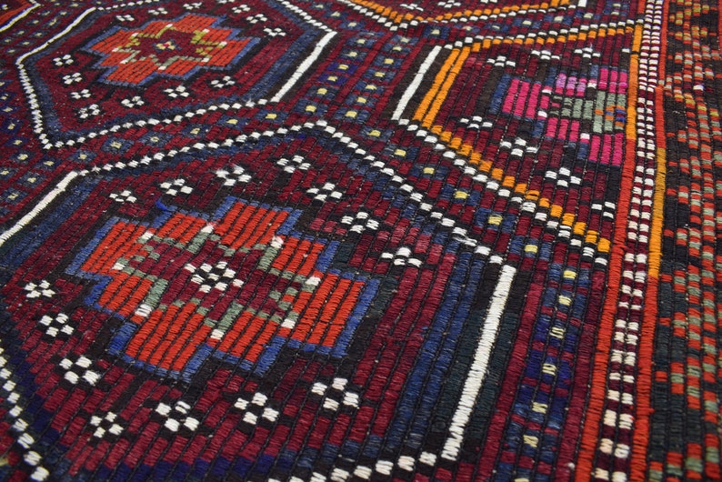 Pu&ograve; includere: Primo piano di un tappeto tessuto colorato con intricati motivi geometrici in tonalit&agrave; di rosso, blu, arancione e bianco.