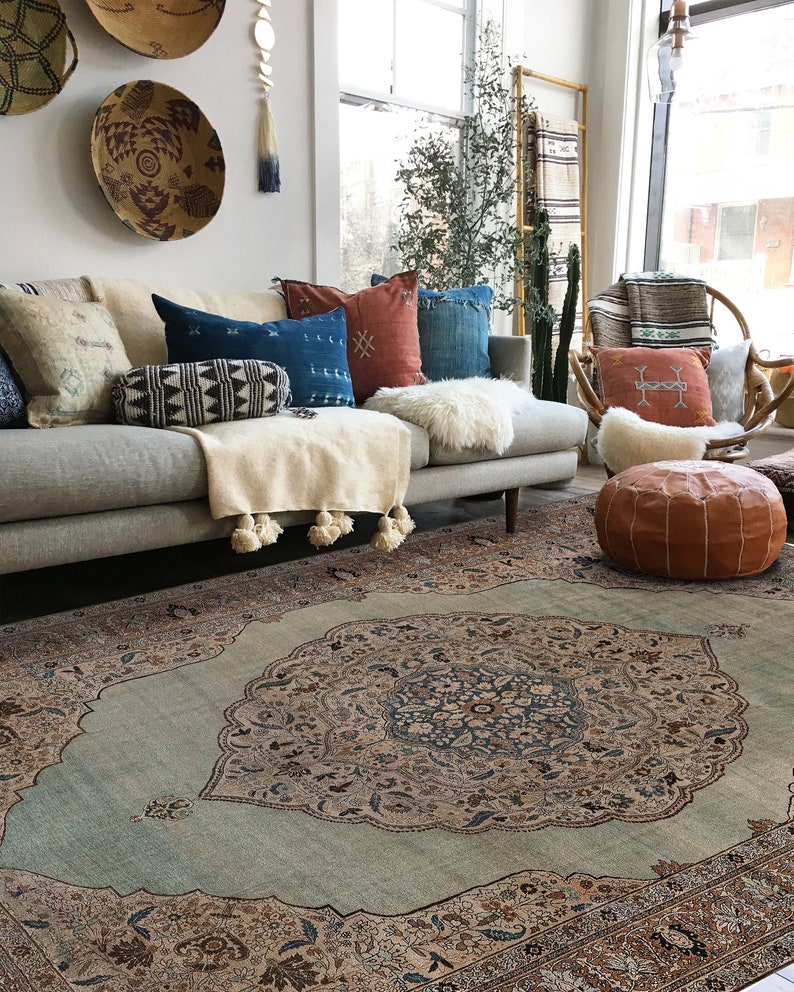 Pu&ograve; includere: Un tappeto blu chiaro con un grande motivo floreale intricato in tonalit&agrave; di marrone, beige e blu. Il tappeto si trova in un soggiorno con un divano grigio e una variet&agrave; di cuscini.